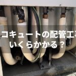 エコキュートの屋外ユニット下部にある配管部分の写真。複数の保温材で覆われた配管が並び、「エコキュートの配管工事いくらかかる？」という文字が重ねて表示されている。